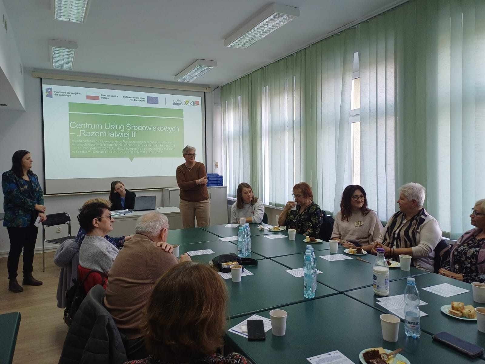 Grupa osób przy stole w tle prezentacja dotyczaca projektu