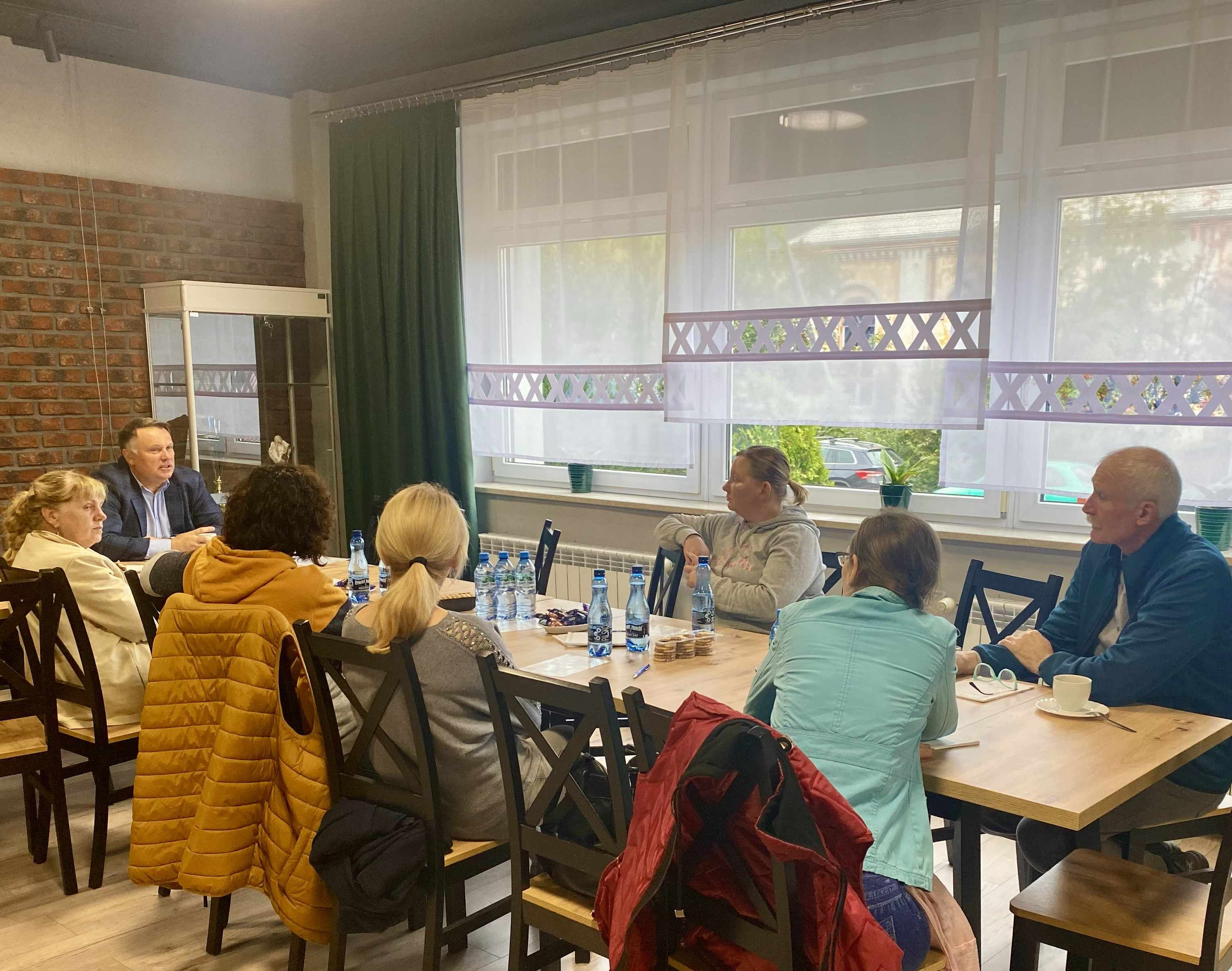 Uczestnicy spotkania siedzą przy stole i słuchają prowadzącego