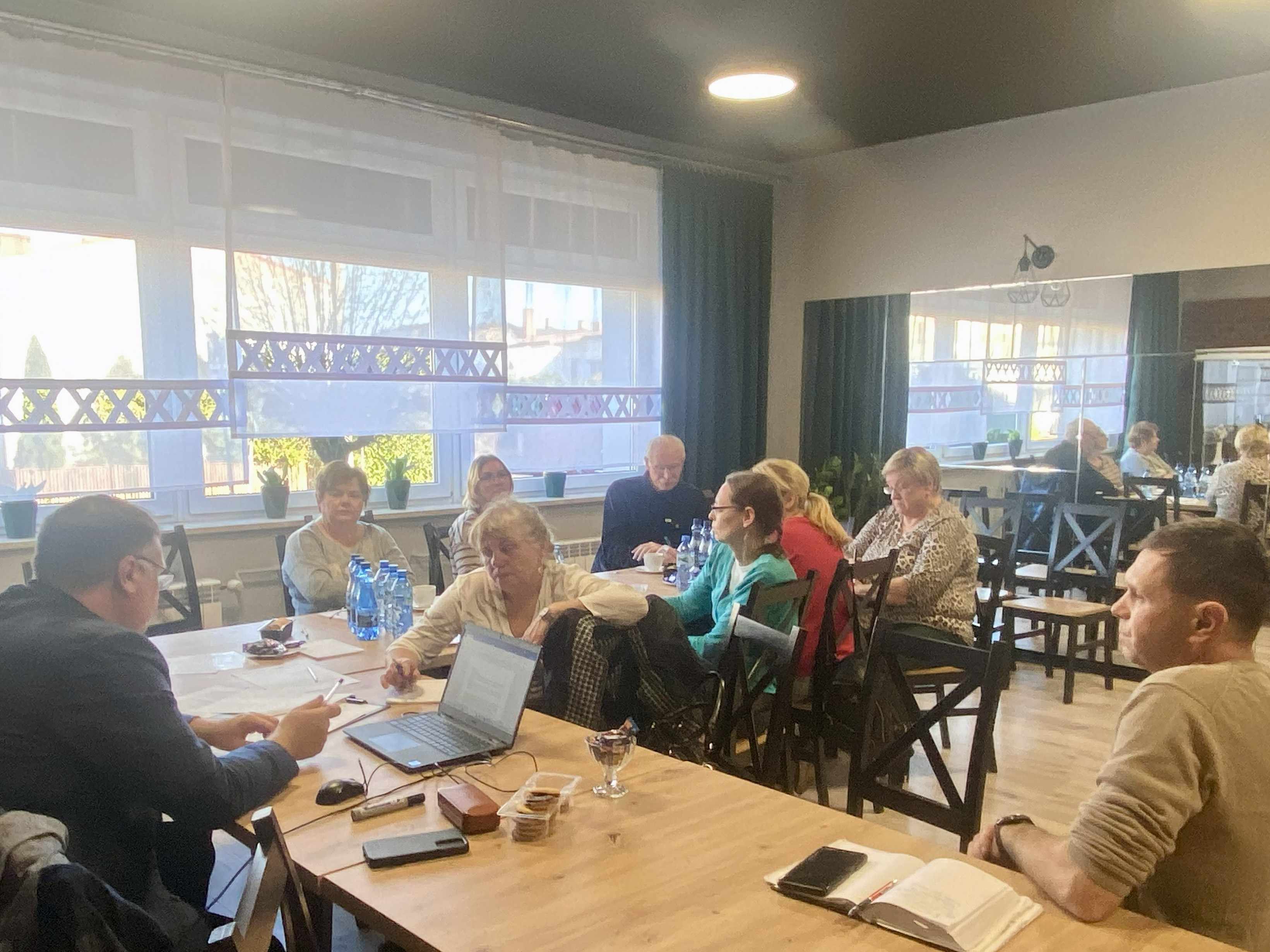 Uczestnicy spotkania siedzą przy stole i słuchają prowadzącego