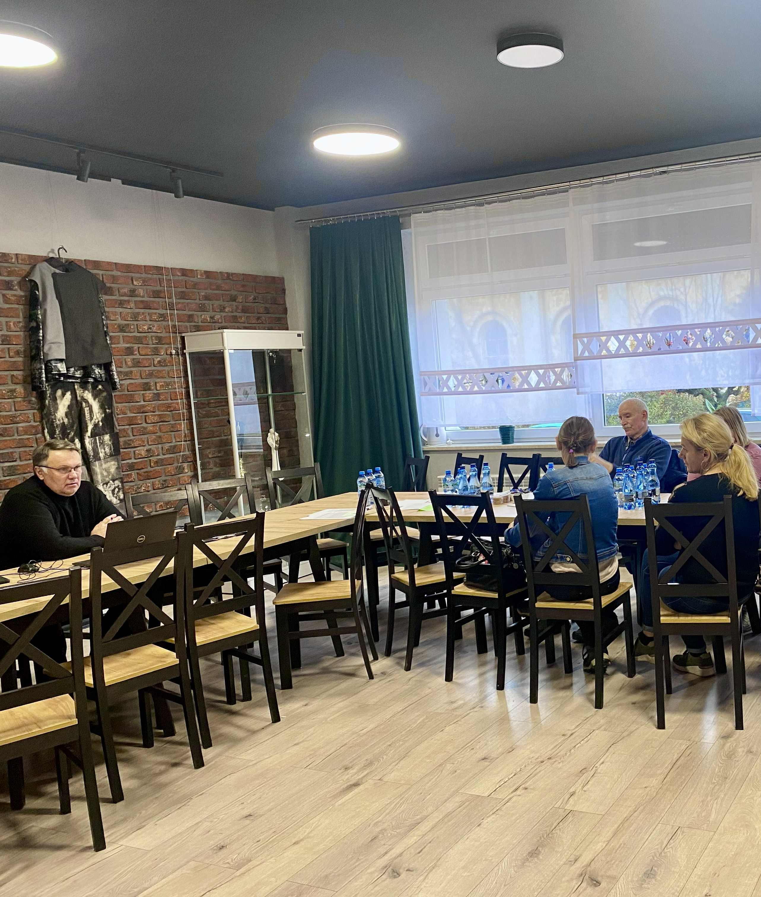 Uczestnicy spotkania siedzą przy stole i słuchają prowadzącego